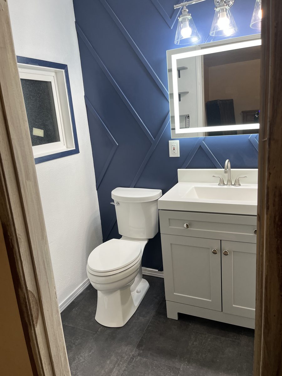 Bathroom with navy geometric accent wall and backlit LED mirror