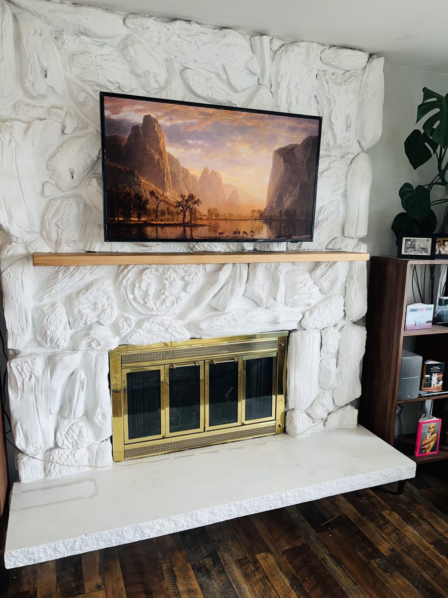 Textured fireplace surround with floating wood mantel and mounted TV