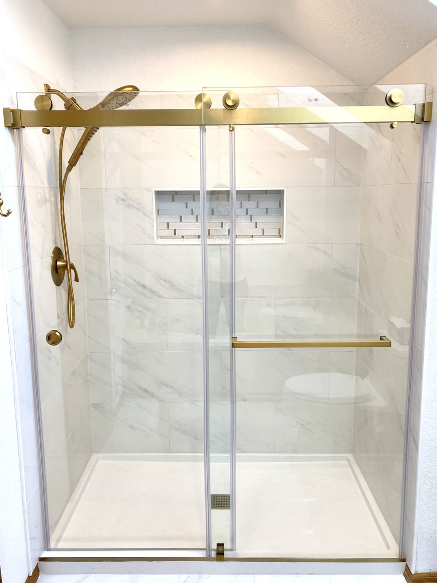 Marble tile shower with brass frameless glass door and inset niche