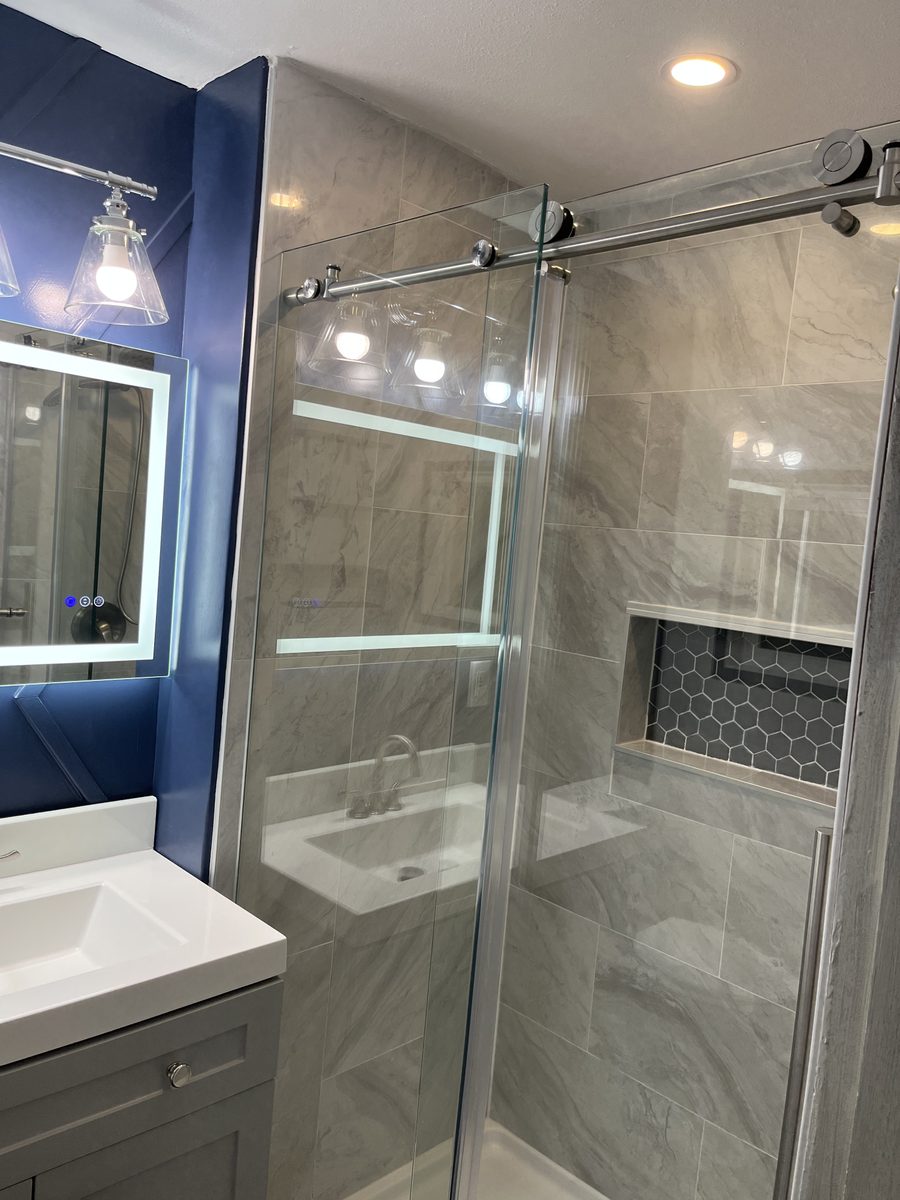 Marble shower with sliding glass door and backlit mirrors