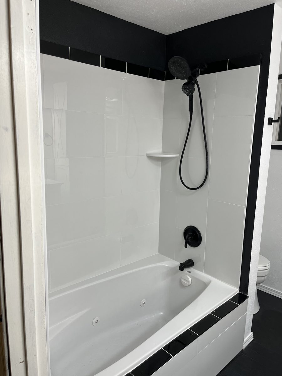 White tub and shower surround with matte black trim and fixtures
